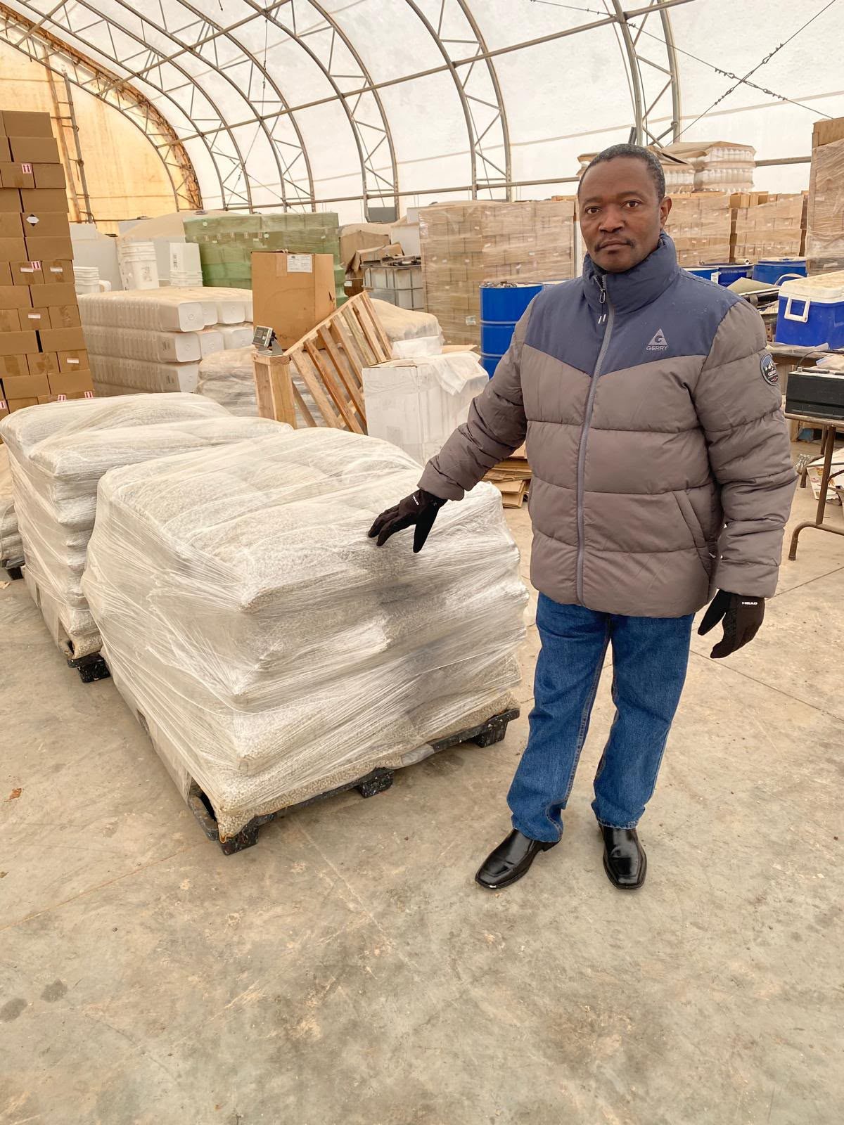 A man beside a wrapped pallet of mineral pellets in a warehouse