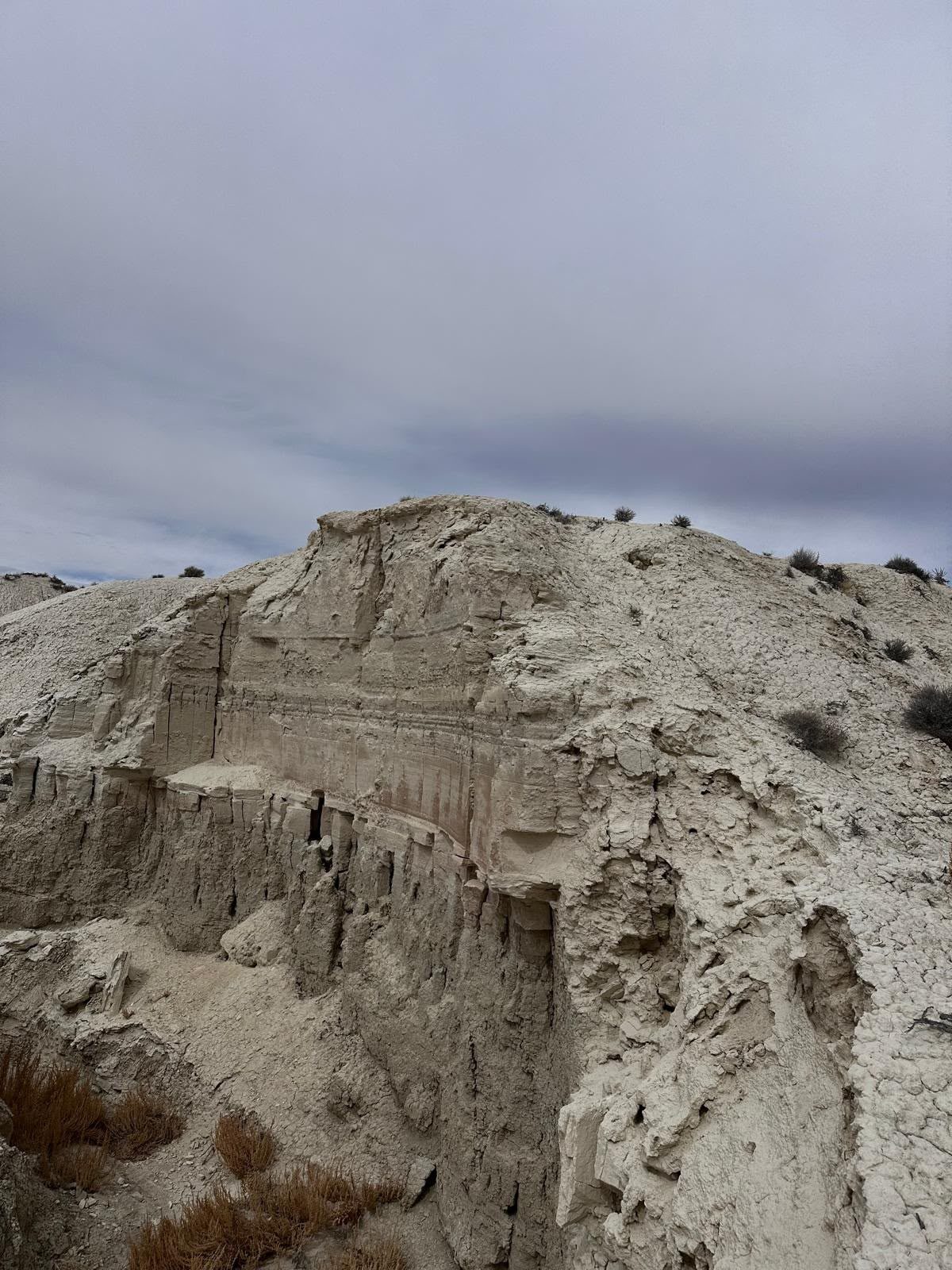 A pale eroded sedimentary cliff under a cloudy sky