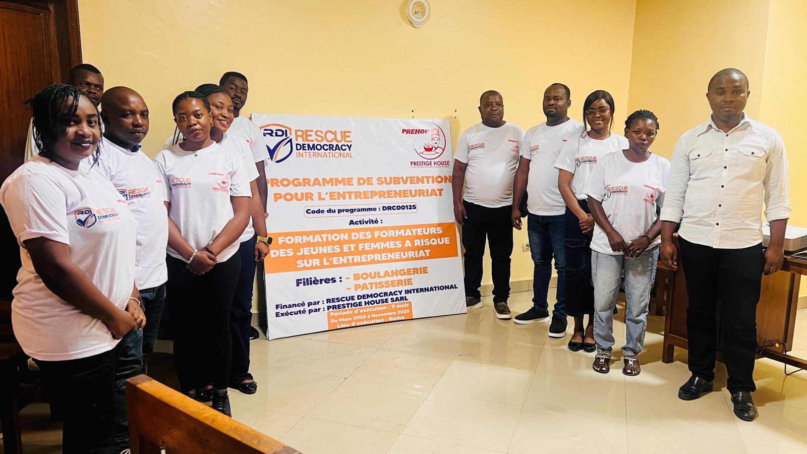 A group in RDI shirts beside a Goma bakery training banner