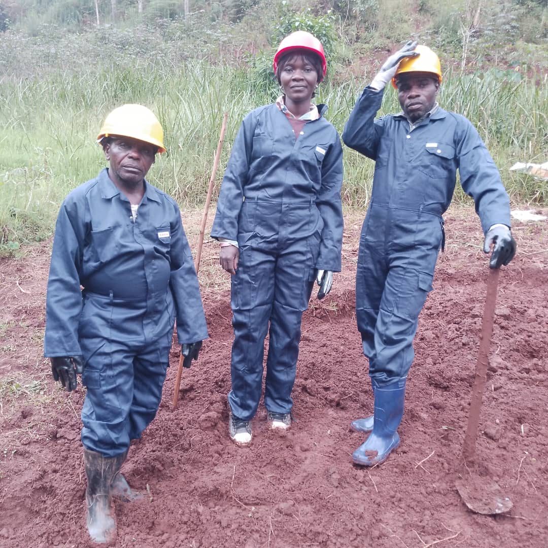 Three workers in coveralls and hard hats standing in red soil