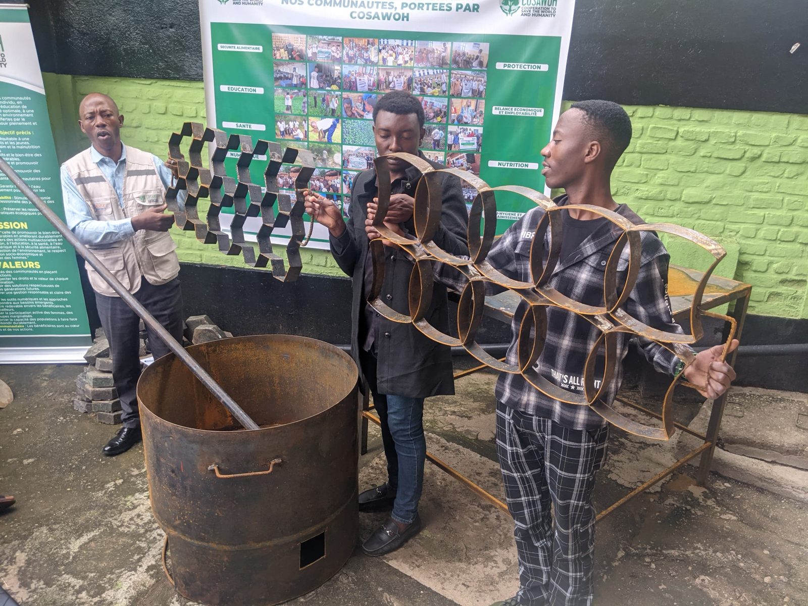 Young men holding metal paver molds beside a melting drum